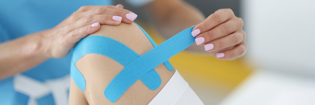 Physiotherapist gluing blue tape on patient knee in clinic closeup