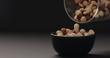 roasted hazelnuts falling into black bowl on black background