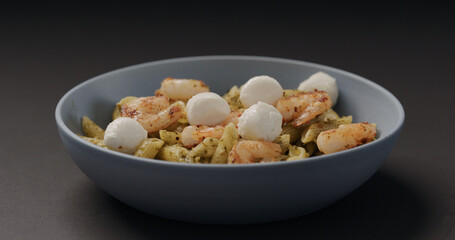 add mozzarella balls to pesto penne with shrimps in blue bowl on black background