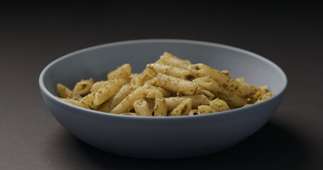 pesto penne in blue bowl on black background