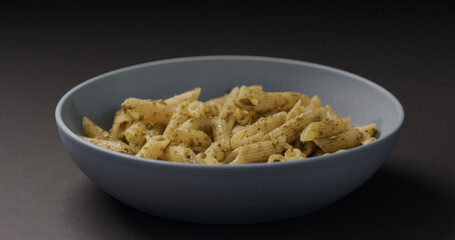 pesto penne in blue bowl on black background
