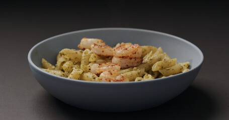 fried shrimps fall on pest penne in blue bowl on black background