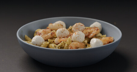 seasoning pesto penne with shrimps and mozzarella in blue bowl on black background