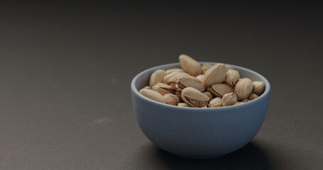 salted pistachios in blue bowl on black background
