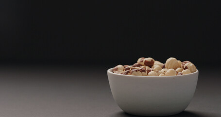 roasted hazelnuts in white bowl on black background