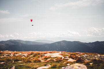 Paraglider silhouette flying over mountains in beautiful summer day. Paraglider flying over a scenic mountainous landscape.
