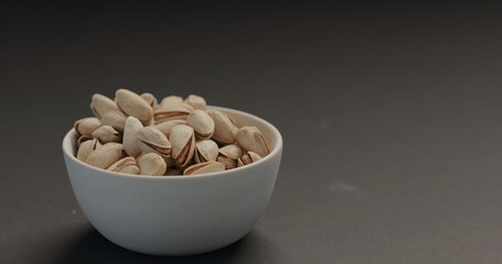salted pistachios in white bowl on black background