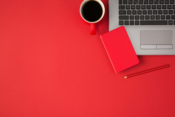 Top view photo of small red closed notebook on laptop red pencil and cup of drink on isolated red...