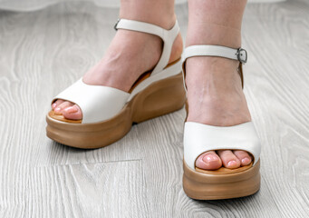 Female feet with White leather sandals stand on floor in the room