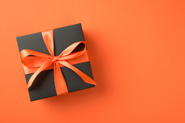 Top view photo of black giftbox with orange satin ribbon bow on isolated orange background with...