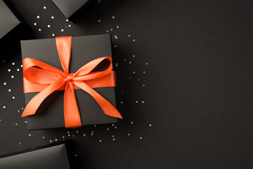 Top view photo of stylish black gift boxes with orange ribbon bow and sequins on isolated black...
