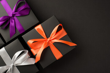 Top view photo of three black gift boxes with violet orange and white satin ribbon bows on isolated black background with copyspace
