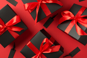 Top view photo of levitating black gift boxes with red ribbon bow and tags on isolated red background with copyspace