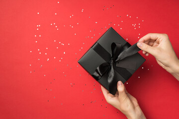 First person top view photo of female hands unpacking stylish black giftbox with black ribbon bow...