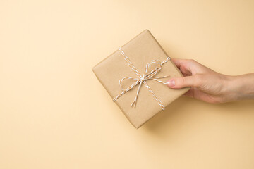 First person top view photo of female hand holding craft paper giftbox with twine bow on isolated...