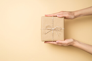 First person top view photo of hands holding stylish craft paper giftbox with twine bow on isolated...