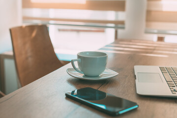 Coffee cup on home office desk between laptop computer and mobile smart phone