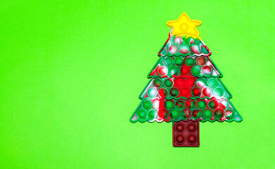 Poppit antistress toy in the form of a Christmas tree on a green background with copy space. New year card or banner