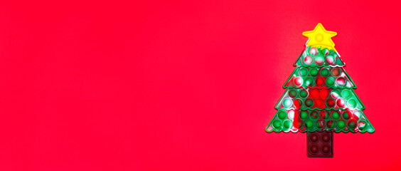 Toy Pop it antistress in the form of a Christmas tree on a red background with copy space. New year banner