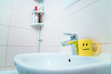 chromed metal faucet for hot and cold water,  cup with sad face for toothbrushes  in a modern bathroom