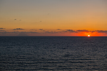 Z prawej strony zachodzące słońce a z lewej widoczny wulkan Stromboli - obrazy, fototapety, plakaty
