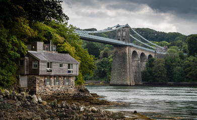 Menai suspension bridge in North Wales with boathouse in foreground on a gloomy day