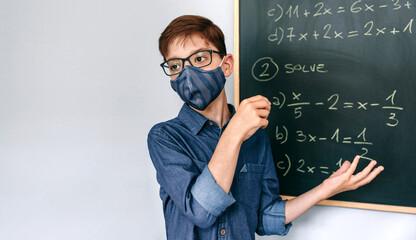 Boy with mask solving math exercises on blackboard at school