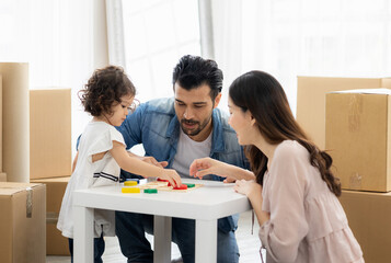 Parents and daughters play with wooden blocks sitting on the floor in the living room at home. The family just moved to a new house. Happy moment Multi-ethnic dad mom and child.