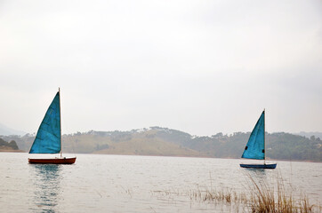 Foggy weather landscape with mountains and boats. Two sailing yachts in the lake leaving the...