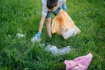 A seven-year-old boy at sunset is engaged in garbage collection in the park. Environmental care,...