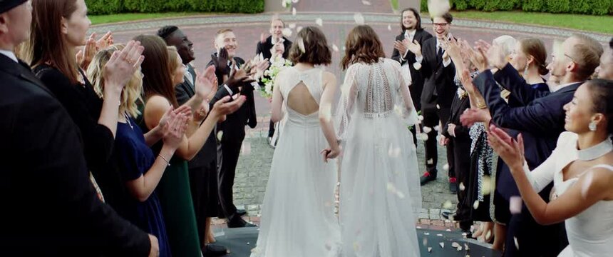Candid shot of two female lesbian LGBT brides walking down the stairs during their wedding ceremony as guests throwing rose petals. Shot with 2x anamorphic lens