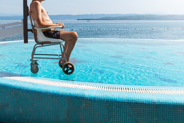 Disabled man on pool wheelchair lift and transferred into water by an assistant.