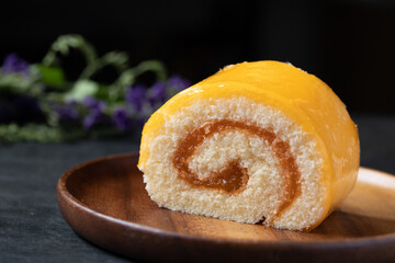 Orange roll cake in wooden plate on black background