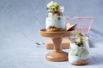 Kiwi yogurt in a glass jar on a gray background.