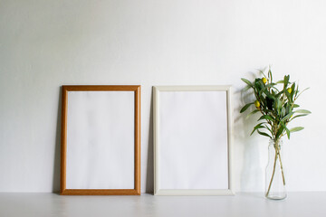Two white frames with leaves on a white wall with nature light. 