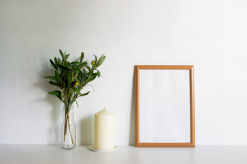 A frame with candles and leaves on a white wall with nature light. 