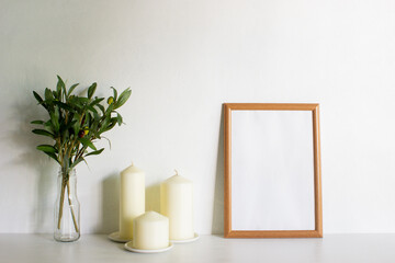 A frame with candles and leaves on a white wall with nature light. 