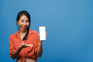 Young Asia lady show empty smartphone screen with positive expression, smiles broadly, dressed in...