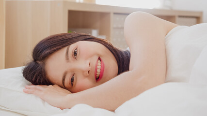 Obraz premium Asian woman smiling lying on bed in bedroom, Beautiful japanese female using relax time after wake up at home. Lifestyle women using relax time at home concept.