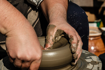Hands of a potter shaping a clay pot on a potter wheel
