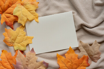 close up top view white blank paper page with group of dried orange color maple leaves on ripple fabric background texture for autumn season collection design concept	
