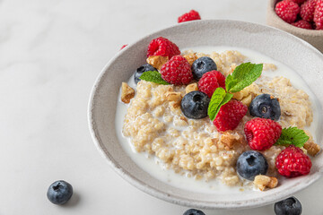 Quinoa porridge with fresh blueberry, raspberry, walnuts and mint in a bowl on white background. close up. healthy breakfast