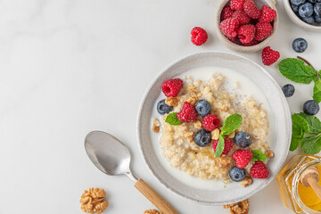 Healthy breakfast. Quinoa porridge with fresh berries, nuts and mint in a bowl with spoon on white background. top view