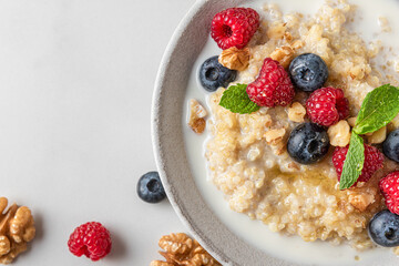 Quinoa porridge with fresh blueberry, raspberry, walnuts, honey and mint in a bowl on white background. top view