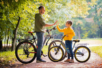 Obraz premium Happy father and daughter walk with bicycles in the autumn park on a sunny day.