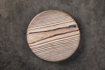 Top view on round burnt wooden serving board on a gray background