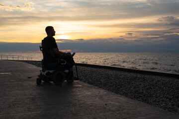 Fototapeta na wymiar Disabled person in a wheelchair at sunset looking at sea.
