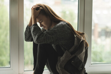 bullying student,sad depressed teen girl sitting on the window,suffers from peer hatred