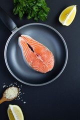 Top view of raw fish salmon in a frying pan on the black background.                 Close-up. Location vertical.