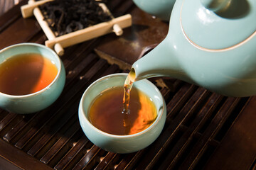 black tea in a teapot is poured into cups. - obrazy, fototapety, plakaty